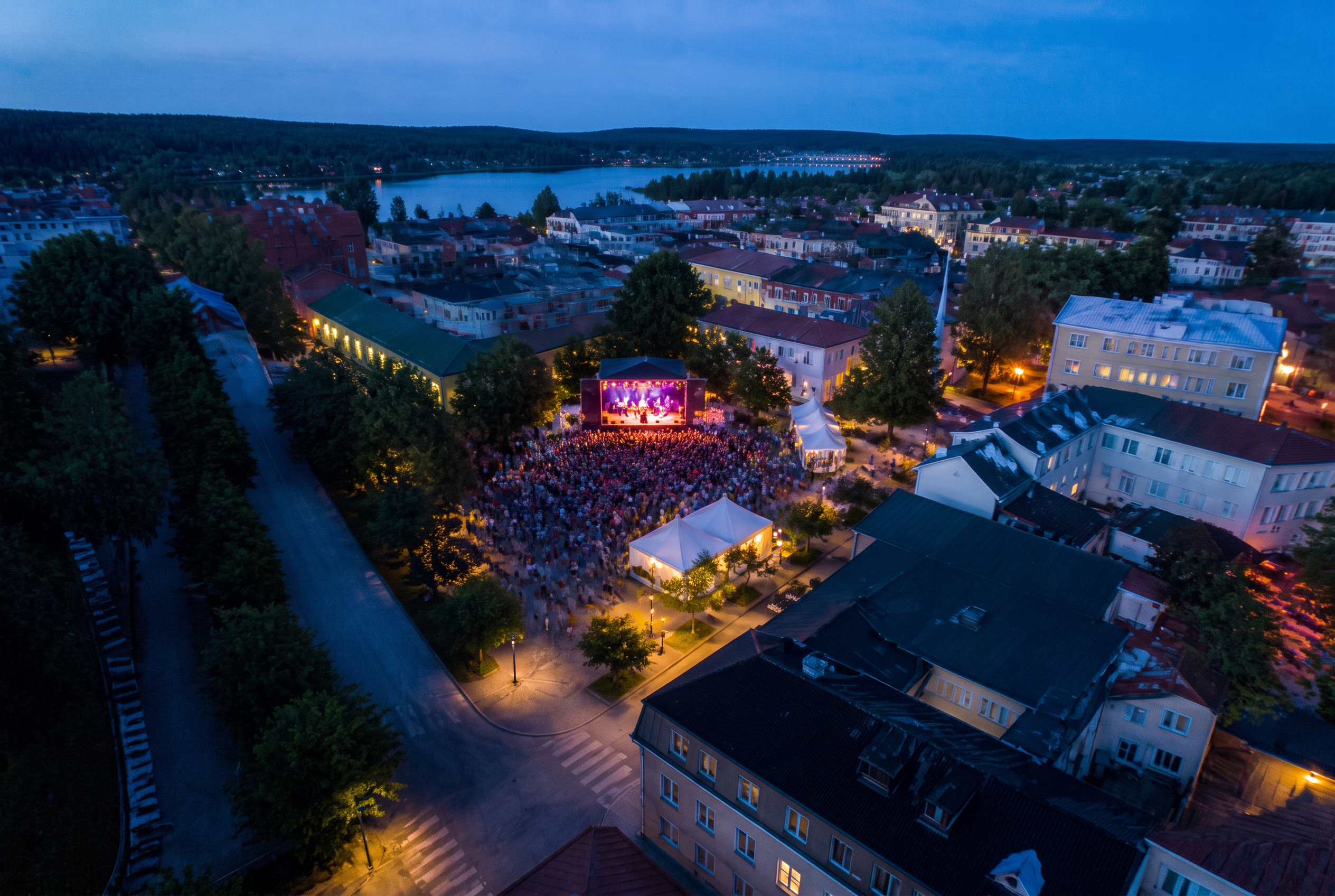 Drönarvy över utomhusevenemang med scen och publik i en svensk stad under blå timmen